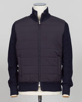 A dark navy blue jacket with a quilted body and ribbed knit sleeves, collar, and hem, displayed on a mannequin against a light gray background. talian wool craftsmanship meets contemporary tailoring in this Gran Sasso sartorial padded jacket. Structured in premium wool with subtle padding for refined warmth, it pairs effortlessly with business wear or elevated casual styling. Gran Sasso Sartorial Padded &nbsp;Wool Jacket / Navy
