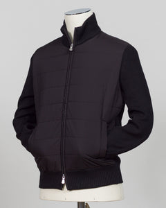 A black zip-up jacket with a quilted front panel and ribbed knit sleeves, collar, and hem, displayed on a mannequin torso against a light gray background. Italian wool craftsmanship meets contemporary tailoring in this Gran Sasso sartorial padded jacket. Structured in premium wool with subtle padding for refined warmth, it pairs effortlessly with business wear or elevated casual styling. Gran Sasso Sartorial Padded &nbsp;Wool Jacket / Black