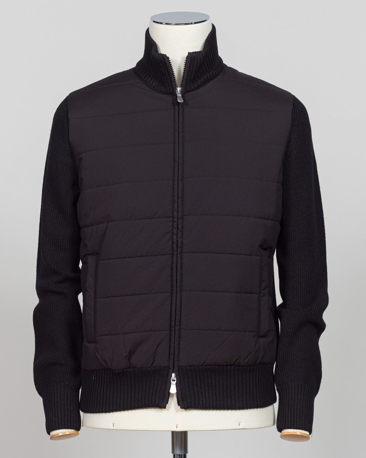 A black mixed-media jacket with a quilted body and ribbed knit sleeves, collar, and hem, displayed on a mannequin torso against a light gray background. Italian wool craftsmanship meets contemporary tailoring in this Gran Sasso sartorial padded jacket. Structured in premium wool with subtle padding for refined warmth, it pairs effortlessly with business wear or elevated casual styling. Gran Sasso Sartorial Padded &nbsp;Wool Jacket / Black