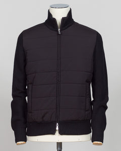 A black mixed-media jacket with a quilted body and ribbed knit sleeves, collar, and hem, displayed on a mannequin torso against a light gray background. Italian wool craftsmanship meets contemporary tailoring in this Gran Sasso sartorial padded jacket. Structured in premium wool with subtle padding for refined warmth, it pairs effortlessly with business wear or elevated casual styling. Gran Sasso Sartorial Padded &nbsp;Wool Jacket / Black