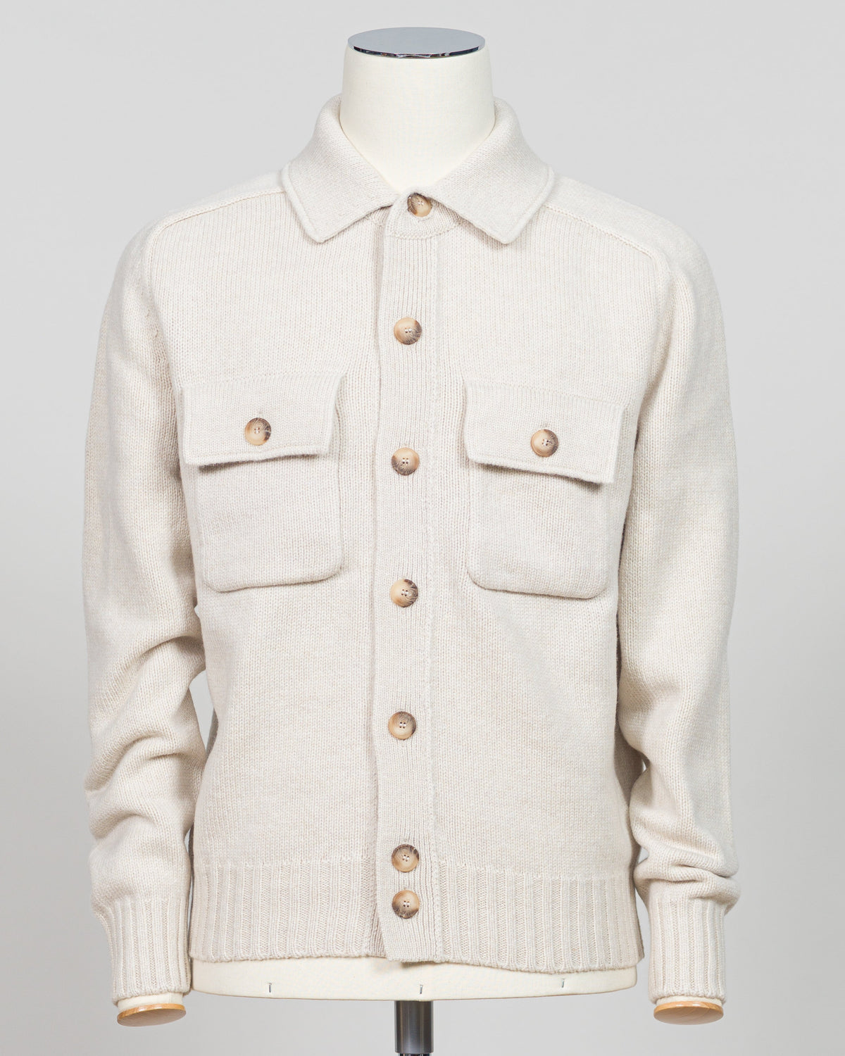 An off-white knit cardigan sweater with brown buttons, displayed on a cream-colored mannequin against a light gray background.