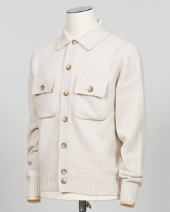A cream-colored knit button-up cardigan sweater with flap chest pockets and wooden buttons, displayed on a mannequin torso against a light gray background.