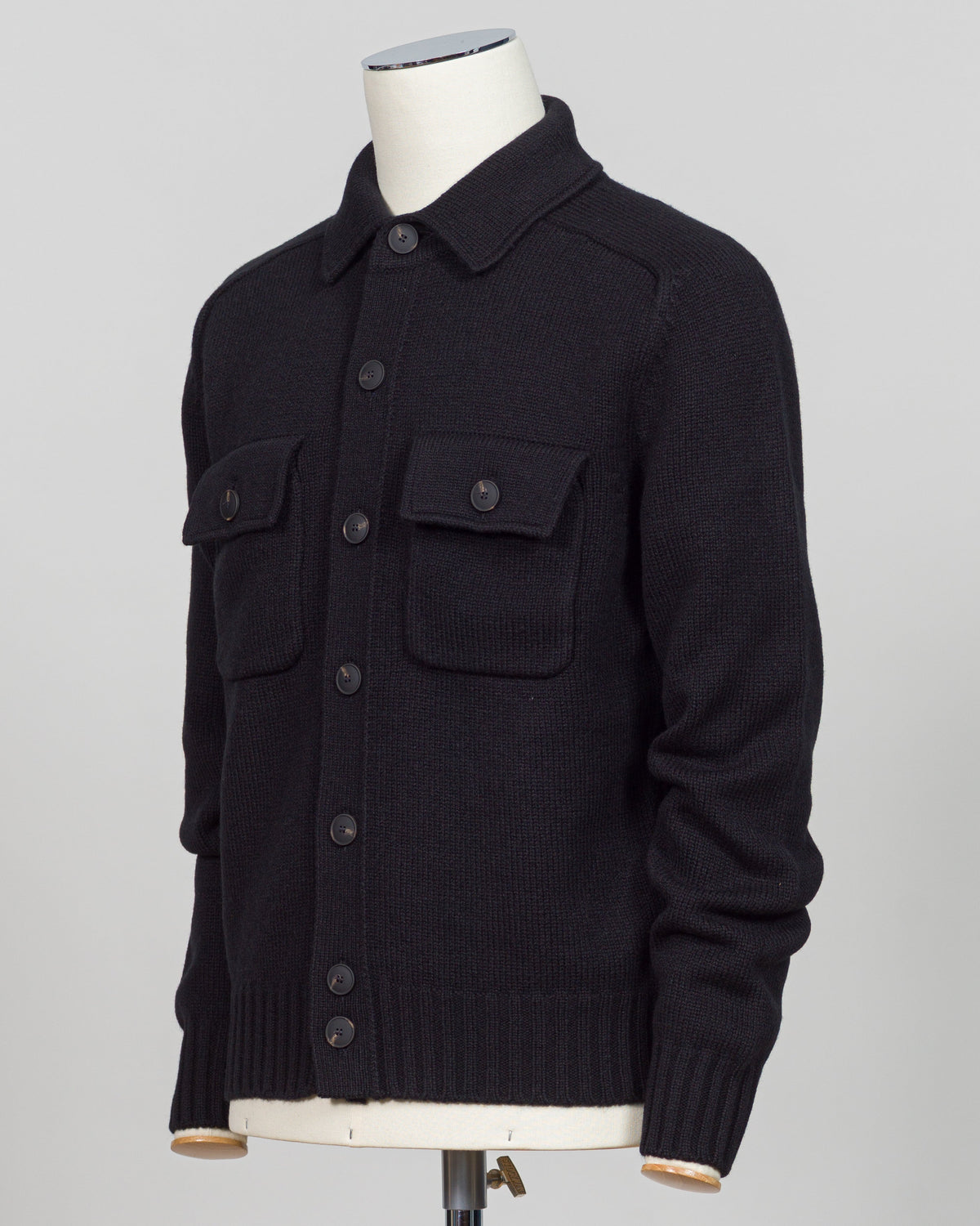 A black knit button-front cardigan sweater with two chest flap pockets, displayed on a white mannequin torso against a light gray studio background.