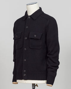 A black knit button-front cardigan sweater with two chest flap pockets, displayed on a white mannequin torso against a light gray studio background.