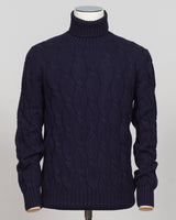 A dark navy blue cable-knit turtleneck sweater displayed on a mannequin torso against a light gray background. A timeless cable knit roll neck in deep navy. Crafted with refined construction, this piece layers effortlessly under tailored jackets or stands alone as an essential foundation for classic menswear. The textured cable pattern adds subtle depth while maintaining the understated elegance expected of premium knitwear. Gran Sasso Cable Roll Neck Knit / Navy
