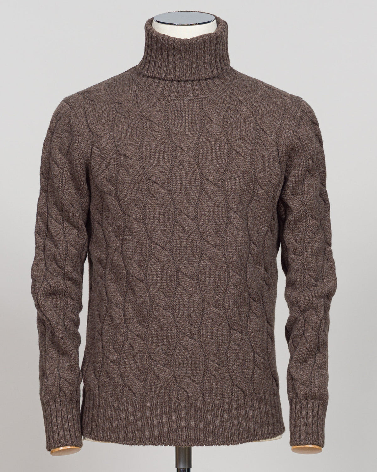 A brown cable-knit turtleneck sweater displayed on a mannequin torso against a light gray background.  Italian wool cable knit roll neck in rich brown. Classic construction with texture and warmth, cut for refined layering under tailored jackets or worn as a standalone piece. Gran Sasso delivers understated luxury in heritage knitwear. Gran Sasso Cable Roll Neck Knit / Brown