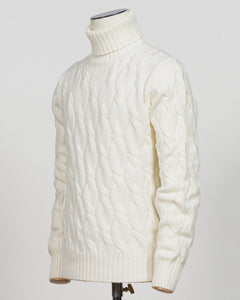 An off-white cable-knit turtleneck sweater displayed on a mannequin torso against a light gray background.  Italian craftsmanship meets timeless elegance in this Gran Sasso cable knit roll neck. Pure white wool construction delivers warmth and refined texture, while the classic silhouette transitions effortlessly from casual to smart-casual layering. A versatile essential for the considered wardrobe. Gran Sasso Cable Roll Neck Knit / White