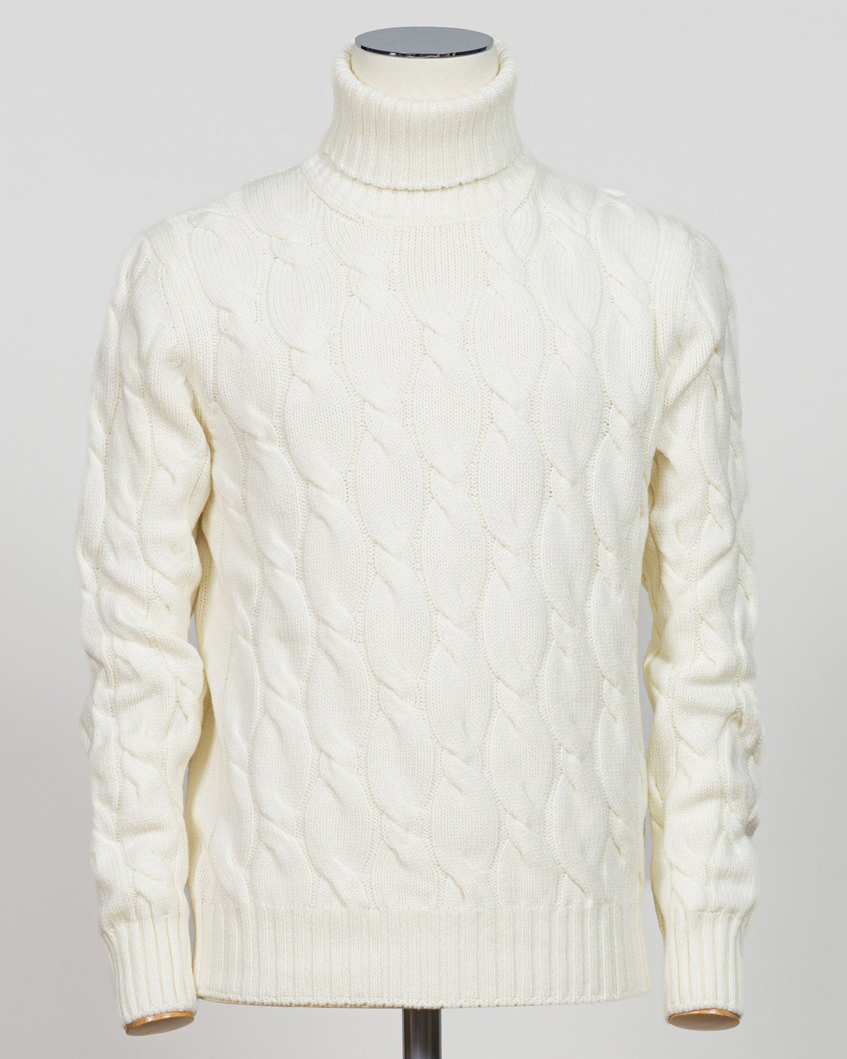 An off-white cable-knit turtleneck sweater displayed on a mannequin torso against a light gray background.  Italian craftsmanship meets timeless elegance in this Gran Sasso cable knit roll neck. Pure white wool construction delivers warmth and refined texture, while the classic silhouette transitions effortlessly from casual to smart-casual layering. A versatile essential for the considered wardrobe. Gran Sasso Cable Roll Neck Knit / White