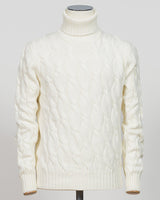 An off-white cable-knit turtleneck sweater displayed on a mannequin torso against a light gray background.  Italian craftsmanship meets timeless elegance in this Gran Sasso cable knit roll neck. Pure white wool construction delivers warmth and refined texture, while the classic silhouette transitions effortlessly from casual to smart-casual layering. A versatile essential for the considered wardrobe. Gran Sasso Cable Roll Neck Knit / White