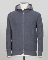 A dark gray ribbed knit zip-up hoodie with a lighter gray hood lining, displayed on a mannequin torso against a neutral light gray Water-repellent merino wool hoodie in warm grey. Engineered for layering and everyday wear, this Gran Sasso piece combines breathable warmth with practical weather resistance. Perfect for transitional seasons and active lifestyles. Gran Sasso Rain Wool Hoodie / Greybackground.
