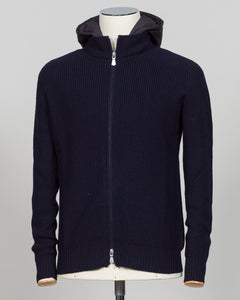 A dark navy blue ribbed knit zip-up hoodie with a hood, displayed on a mannequin torso against a light gray background. Water-repellent merino wool hoodie in navy. Engineered for layering and everyday wear, this Gran Sasso piece combines breathable warmth with practical weather resistance. Perfect for transitional seasons and active lifestyles. Gran Sasso Rain Wool Hoodie / Navy