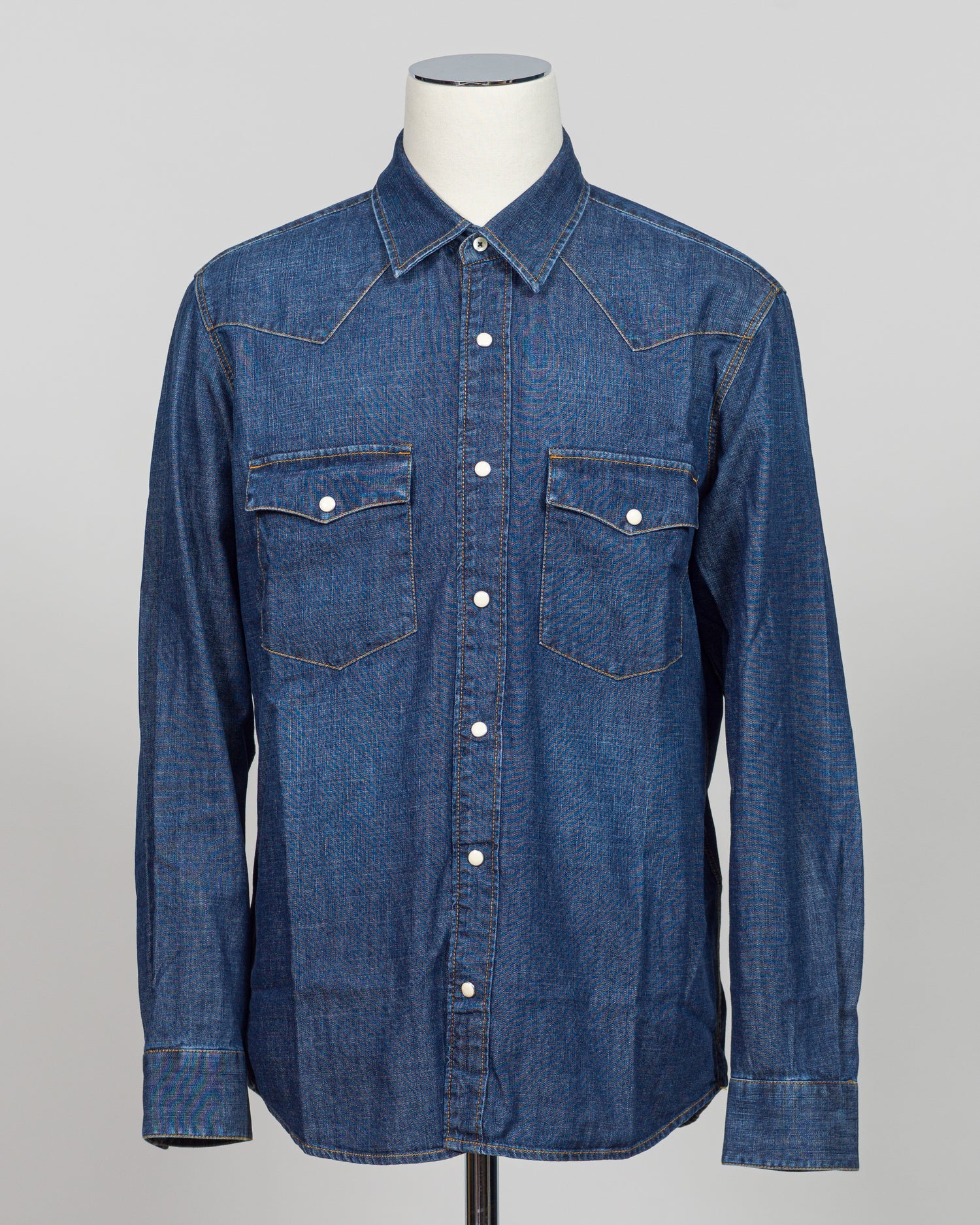 Crafted from premium Tela Genova fabric, this Western shirt delivers understated sophistication in a faded blue that transitions beautifully across seasons. The structured weave and refined tailoring define clean lines, while pearl snaps and a relaxed collar offer versatile styling—equally at home layered under a blazer or worn open as a lightweight layer. Perfect for the discerning dresser who values quality construction and timeless design.