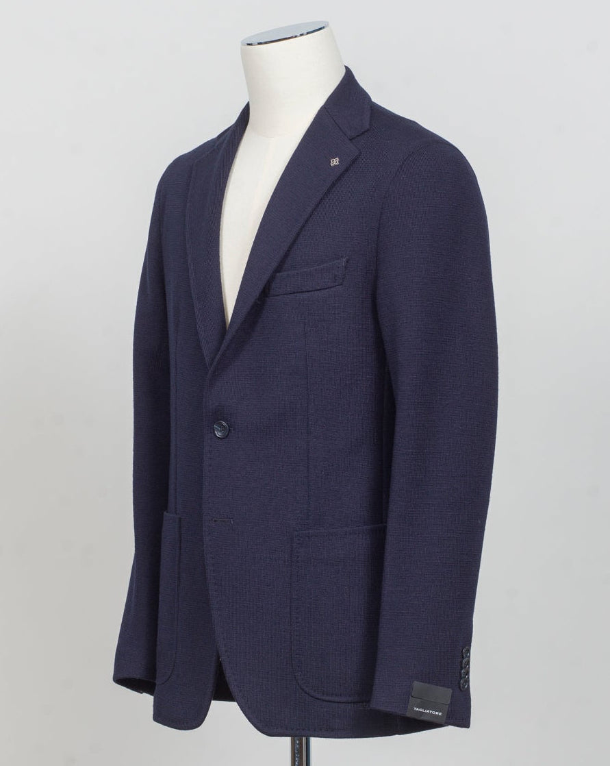 A navy blue single-breasted blazer displayed on a white mannequin torso against a light gray studio background. Tailored jersey jacket in soft navy wool blend. Clean, modern silhouette designed for everyday sophistication. Lightweight construction offers comfort without sacrificing structure. Perfect for layering or wearing solo across seasons. Italian craftsmanship meets versatile styling. Tagliatore Jersey Jacket / Navy