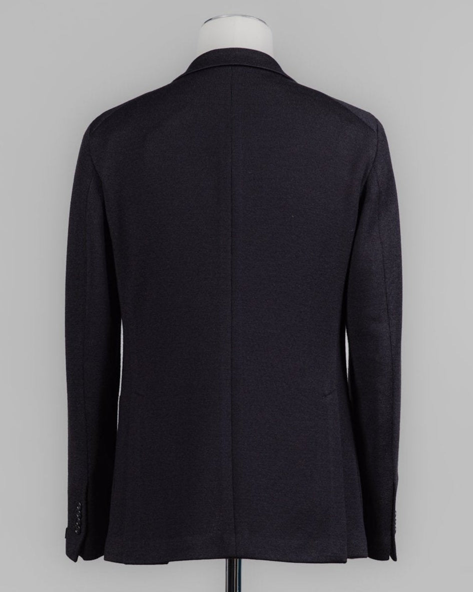 A dark navy blue wool blazer shown from the back on a mannequin torso against a neutral gray background. Tagliatore's refined jersey jacket combines Italian craftsmanship with modern ease. The lightweight knit construction offers comfort and movement, while the structured silhouette maintains a polished appearance. Perfect for layering or wearing solo, this black essential transitions seamlessly from office to weekend. Tagliatore Jersey Jacket / Black