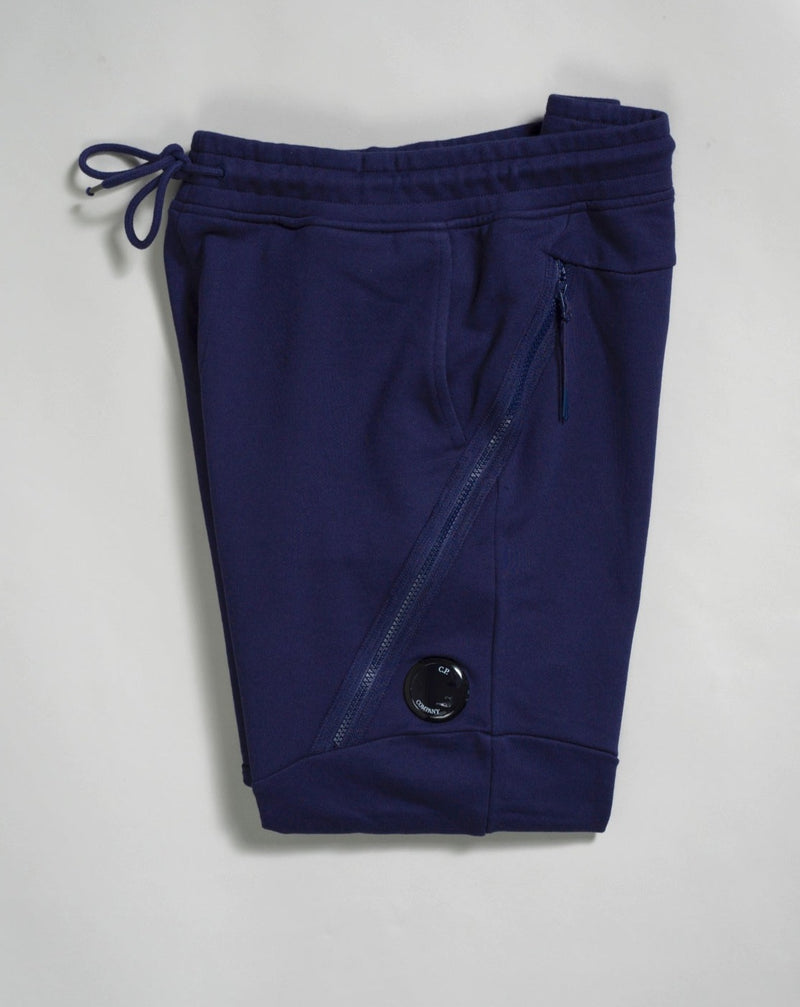 Sweatpants with an adjustable drawstring waistband and tapered legs. The sweatpants also feature slanted hand pockets and a C.P. Company Lens detail on the left leg. Crafted in diagonal raised fleece, a midweight loopback cotton option that combines absolute comfort with a substantial and hard-wearing feel.  14CMSP084A005086W Col 868 Medieval Blue Adjustable drawstring waistband Slanted hand pockets Angular thigh zip pockets Lens detail Tapered leg