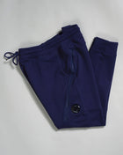 Sweatpants with an adjustable drawstring waistband and tapered legs. The sweatpants also feature slanted hand pockets and a C.P. Company Lens detail on the left leg. Crafted in diagonal raised fleece, a midweight loopback cotton option that combines absolute comfort with a substantial and hard-wearing feel.  14CMSP084A005086W Col 868 Medieval Blue Adjustable drawstring waistband Slanted hand pockets Angular thigh zip pockets Lens detail Tapered leg