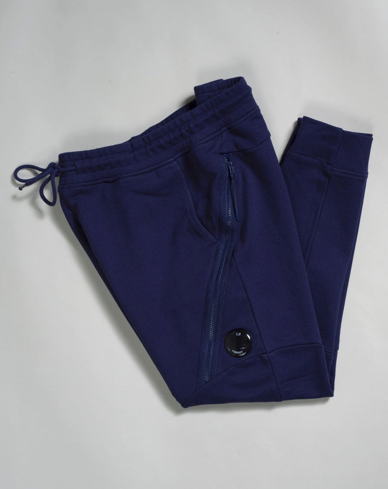 Sweatpants with an adjustable drawstring waistband and tapered legs. The sweatpants also feature slanted hand pockets and a C.P. Company Lens detail on the left leg. Crafted in diagonal raised fleece, a midweight loopback cotton option that combines absolute comfort with a substantial and hard-wearing feel.  14CMSP084A005086W Col 868 Medieval Blue Adjustable drawstring waistband Slanted hand pockets Angular thigh zip pockets Lens detail Tapered leg