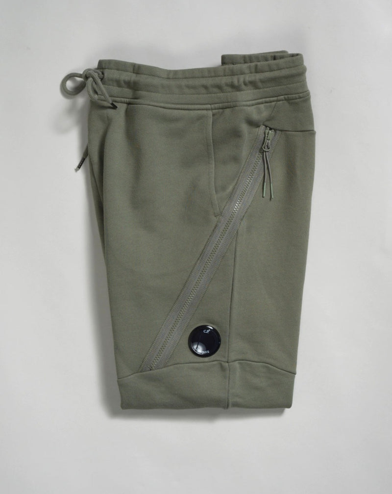 Sweatpants with an adjustable drawstring waistband and tapered legs. The sweatpants also feature slanted hand pockets and a C.P. Company Lens detail on the left leg. Crafted in diagonal raised fleece, a midweight loopback cotton option that combines absolute comfort with a substantial and hard-wearing feel.  14CMSP084A005086W Col 648 Bronze Green Adjustable drawstring waistband Slanted hand pockets Angular thigh zip pockets Lens detail Tapered leg