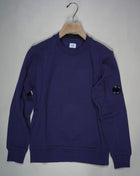 Crewneck sweatshirt featuring the C.P. Company Lens on the sleeve pocket. Manufactured in our diagonal raised fleece, a midweight loopback cotton option that combines absolute comfort with a substantial and hard-wearing feel. Art. SP084A 5086W Col. 868 Medieval Blue Ribbed Cuffs, Hem and Neck Lens Detail Sleeve Pocket Logo Detail Back Collar