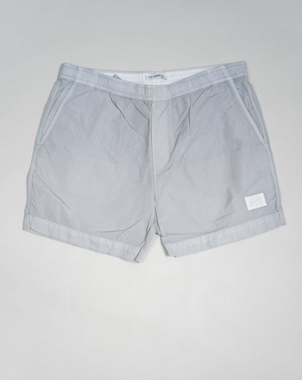 Eco-Chrome swim shorts constructed with an elasticated drawstring waist, hand pockets and a logo detail. Chrome is C.P. Company’s foundation woven multifilament nylon. This new version uses Econyl® regenerated nylon yarns, created through the upcycling of fishing nets.  Art.  BW005A 6369G Col.  936 Light Gray Elasticated drawstring waist Hand pockets Logo detail Nylon dyed 