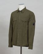 A buttoned shirt featuring a classic collar, secure pockets at the chest, and a discreet sleeve compartment finished with the C.P. Company Lens detail.  Classic Collar Full Button Fastening Secure Chest Pockets Lens Detail Sleeve Pocket Col. 683 / Ivy Green 100% Cotton Art. 12CMSH088A 002824G