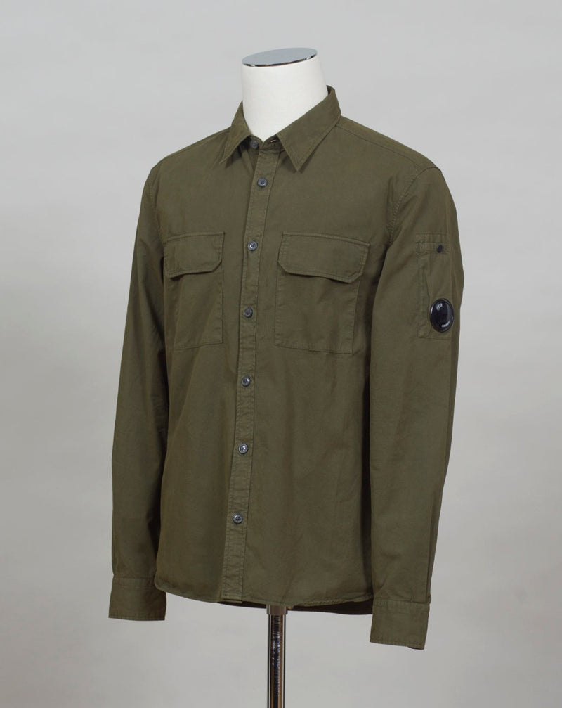A buttoned shirt featuring a classic collar, secure pockets at the chest, and a discreet sleeve compartment finished with the C.P. Company Lens detail.  Classic Collar Full Button Fastening Secure Chest Pockets Lens Detail Sleeve Pocket Col. 683 / Ivy Green 100% Cotton Art. 12CMSH088A 002824G