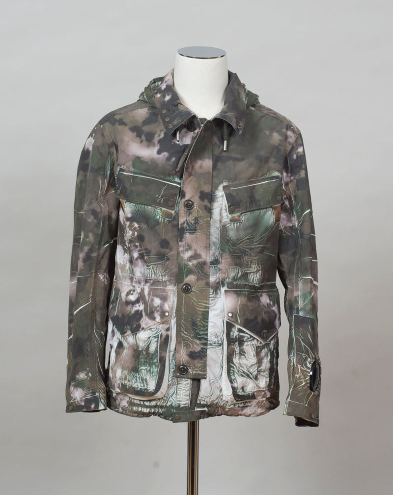 "C.P. Company Tracery Process Woodland Pattern GRN Var Piece No._" Embroidered on back. Every jacket has a different number on it. See the last picture. Woodland Pattern Detachable Goggle Hood Classic Hood Zip and Storm Flap Fastening Secure Hand Pockets Auxiliary Chest Compartments Watch Viewer Lens Detail Sublimation Printed Garment Dyed Col. 660 / Burnt Olive Art. 12CMOW260A 005990P