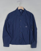 Workwear-inspired long sleeved shirt cut with a classic collar and a full button fastening. The shirt also features an open chest pocket and two open front pockets, adjustable cuffs and a C.P. Company logo detail. Crafted in a crisp cotton poplin with a soft, silken surface, and garment dyed for an increased chromatic depth and intensity throughout. Art. 14CMSH355A 5328G Col. 868 French Blue Cotton Popeline