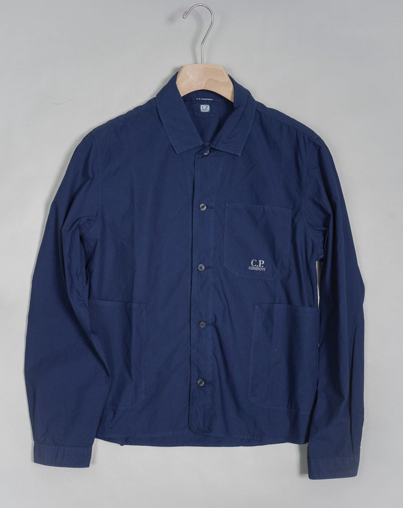 Workwear-inspired long sleeved shirt cut with a classic collar and a full button fastening. The shirt also features an open chest pocket and two open front pockets, adjustable cuffs and a C.P. Company logo detail. Crafted in a crisp cotton poplin with a soft, silken surface, and garment dyed for an increased chromatic depth and intensity throughout. Art. 14CMSH355A 5328G Col. 868 French Blue Cotton Popeline